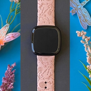 May include: A pink silicone watch band with a floral and dragonfly design. The band is compatible with smartwatches.
