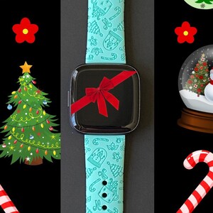 May include: A turquoise smartwatch band with a Christmas-themed design. The band features a variety of festive icons, including candy canes, snowmen, Christmas trees, and ornaments.
