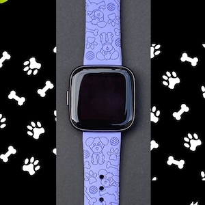 May include: A purple silicone watch band with a pattern of dogs, bones, and paw prints. The band is designed for a smartwatch.