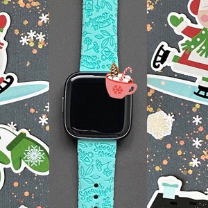 Pu&ograve; includere: Un cinturino per smartwatch blu turchese con un fiocco di neve bianco e un design "Sweater Weather". Il cinturino &egrave; su uno sfondo grigio con vari adesivi a tema invernale, tra cui un pupazzo di neve, una casa e una canna di zucchero.