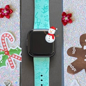 May include: A turquoise blue smartwatch band with a Christmas theme. The band features snowflakes, candy canes, gingerbread men, and snowmen.