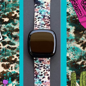 Puede incluir: Un smartwatch con una esfera negra y una banda colorida con un patr&oacute;n de cr&aacute;neo de vaca, herradura, cactus y bota de vaquero. La banda est&aacute; hecha de silicona y tiene un dise&ntilde;o de cierre.