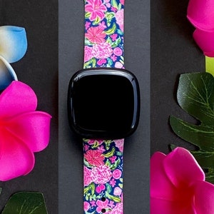 Pu&ograve; includere: Un cinturino per orologio floreale rosa e blu per uno smartwatch. Il cinturino &egrave; in silicone e presenta una stampa floreale. Il cinturino dell'orologio &egrave; mostrato su uno sfondo nero con fiori rosa.