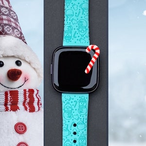 May include: A turquoise blue Apple Watch band with a snowman and candy cane pattern. The band is on a black background.