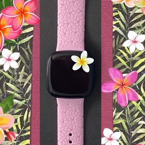 May include: A pink silicone watch band with a black watch face. The band has a floral pattern and the watch face has a black background.