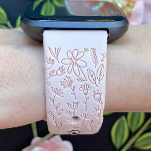 Op de afbeelding: Een roze siliconen horlogebandje met een bloemenpatroon. Het bandje is ontworpen voor een smartwatch met een zwart gezicht.