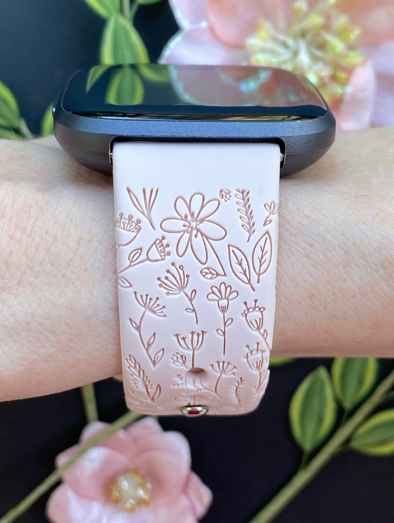 Op de afbeelding: Een roze siliconen horlogebandje met een bloemenpatroon. Het bandje is ontworpen voor een smartwatch met een zwart gezicht.