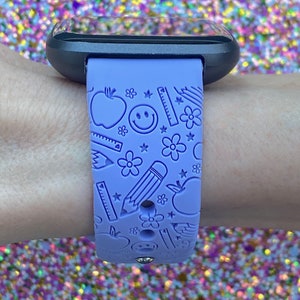 May include: A purple silicone watch band with a school-themed design. The band features a repeating pattern of apples, pencils, rulers, stars, and smiley faces.