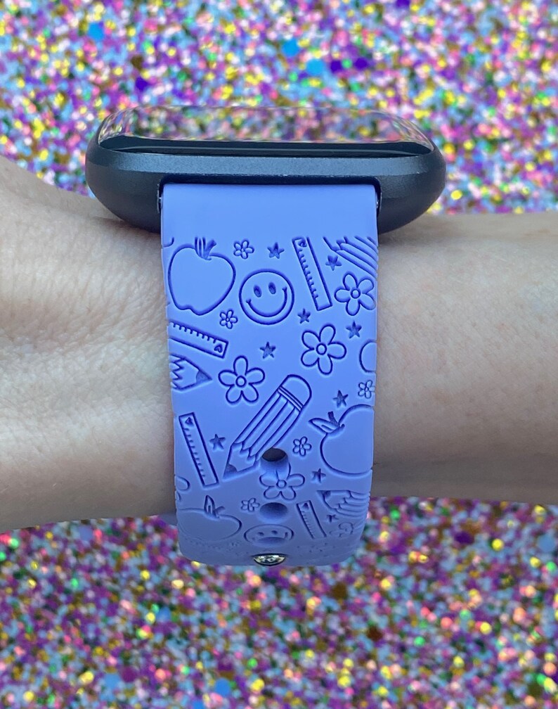 May include: A purple silicone watch band with a school-themed design. The band features a repeating pattern of apples, pencils, rulers, stars, and smiley faces.