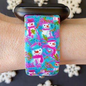 K&ouml;nnte beinhalten: Ein blaues und pinkfarbenes Armband mit einem Schneemannmuster. Das Armband ist aus Silikon und hat einen Metallverschluss.