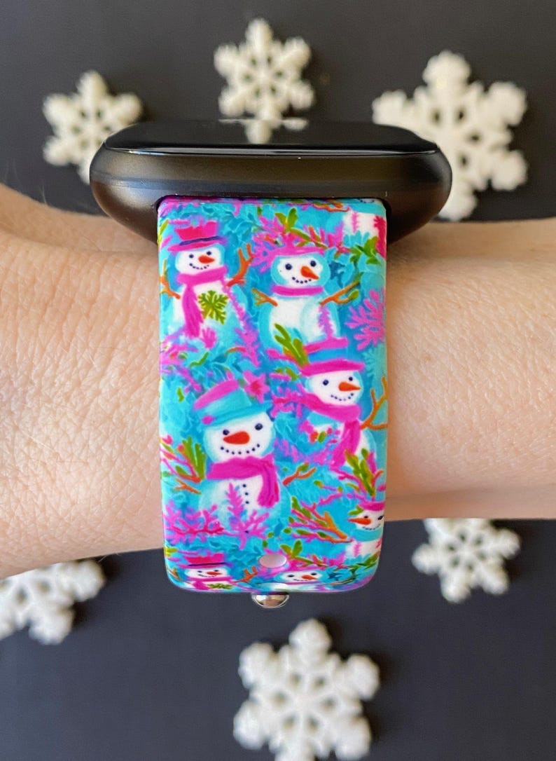 K&ouml;nnte beinhalten: Ein blaues und pinkfarbenes Armband mit einem Schneemannmuster. Das Armband ist aus Silikon und hat einen Metallverschluss.