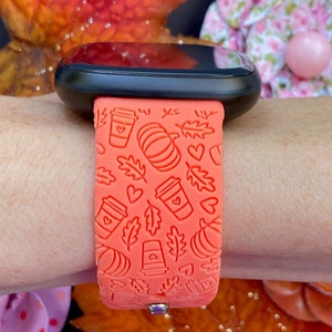 May include: A bright orange silicone watch band with a pattern of coffee cups, pumpkins, leaves, and hearts. The band is designed for a smartwatch.