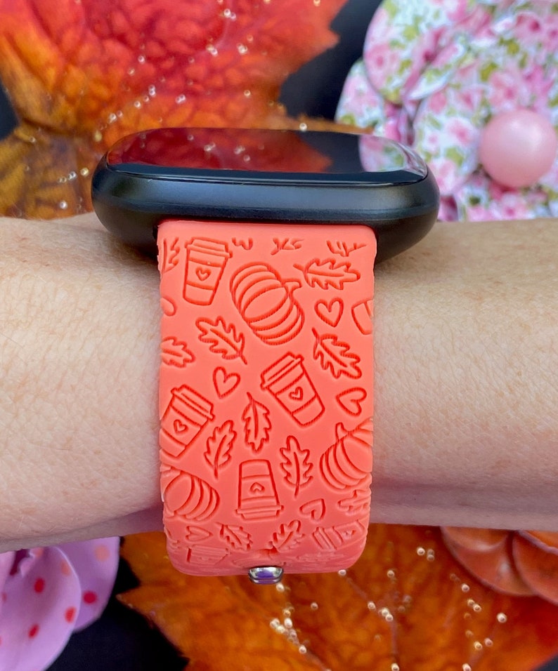 May include: A bright orange silicone watch band with a pattern of coffee cups, pumpkins, leaves, and hearts. The band is designed for a smartwatch.