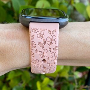 May include: A pink silicone watch band with a floral pattern. The band is designed for a smartwatch with a square face.