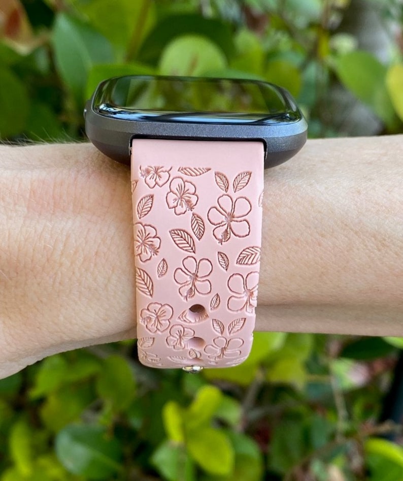 May include: A pink silicone watch band with a floral pattern. The band is designed for a smartwatch with a square face.