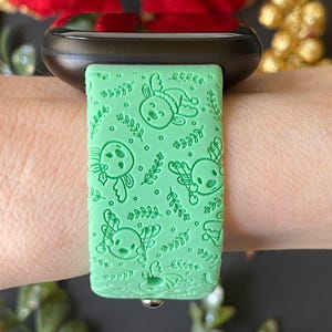 May include: A green silicone watch band with a pattern of reindeer and holly. The band is designed for a smartwatch.