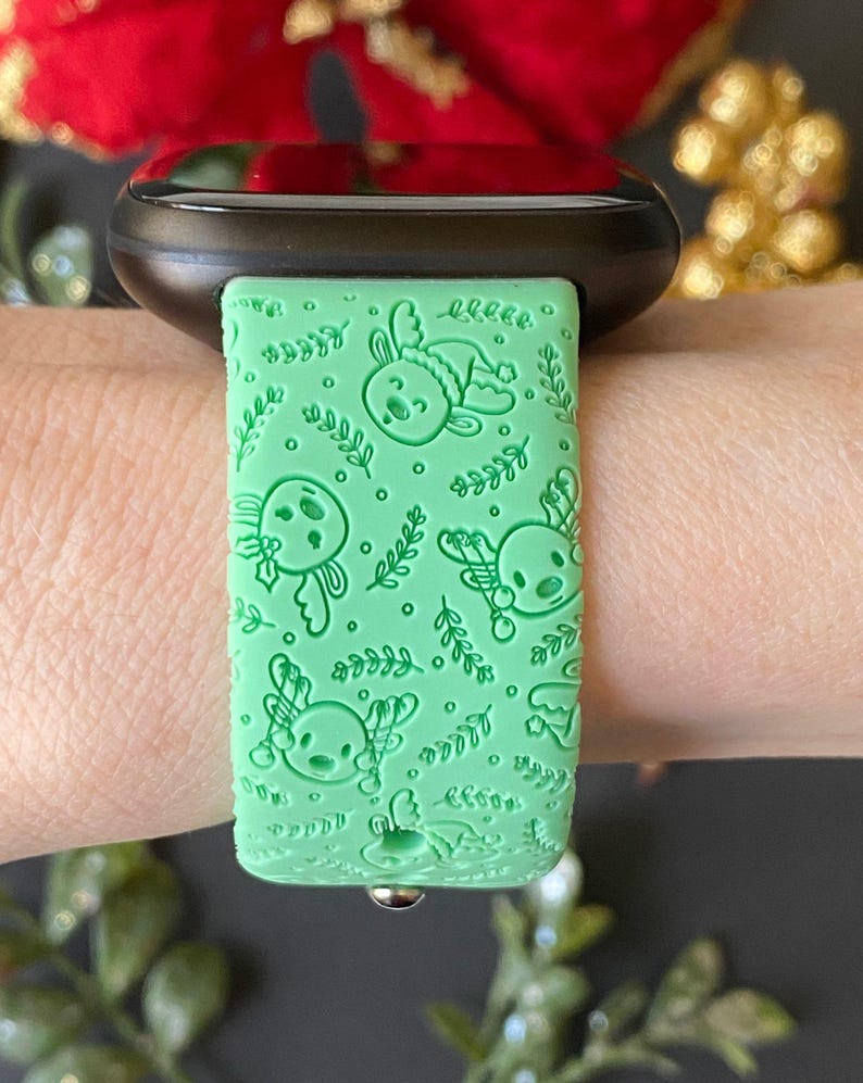 May include: A green silicone watch band with a pattern of reindeer and holly. The band is designed for a smartwatch.
