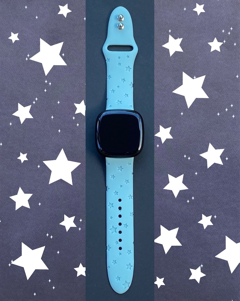 May include: A light blue smartwatch band with a white star pattern. The band is made of silicone and has a buckle closure.