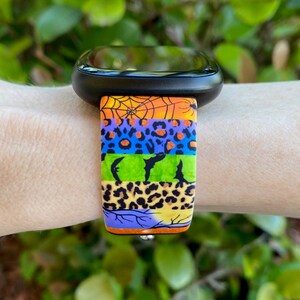 May include: A colorful watch band with a Halloween theme. The band features a spiderweb, bats, and leopard print patterns in orange, green, blue, and purple.