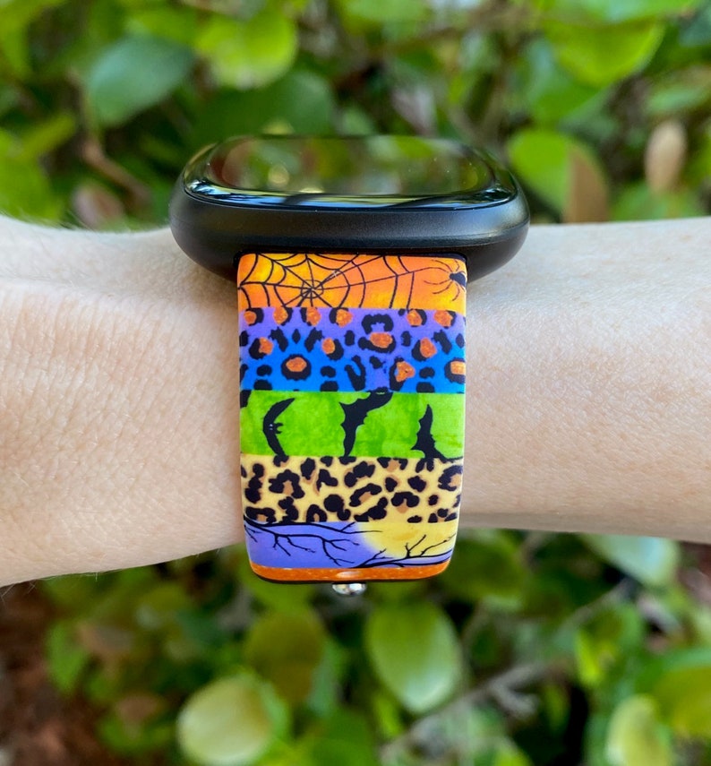 May include: A colorful watch band with a Halloween theme. The band features a spiderweb, bats, and leopard print patterns in orange, green, blue, and purple.