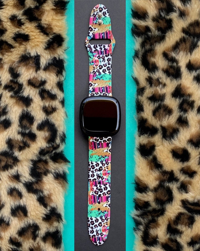 May include: A black smartwatch with a colorful leopard print band. The band has a white background with pink, blue, green, and gold accents.