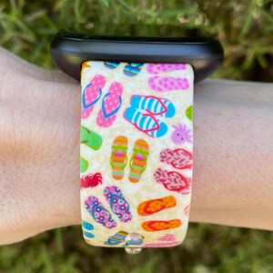 May include: A white watch band with a colorful print of flip flops. The band is made of silicone and has a black watch face.