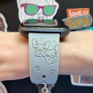 May include: A light gray smartwatch band with a black watch face. The band has a design of two French Bulldogs with hearts and paw prints.
