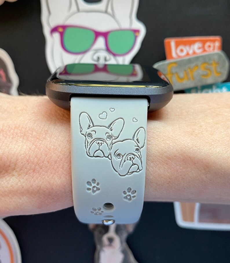 May include: A light gray smartwatch band with a black watch face. The band has a design of two French Bulldogs with hearts and paw prints.