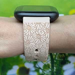 May include: A pink silicone watch band with a daisy pattern. The band is worn on a wrist and has a black watch face.