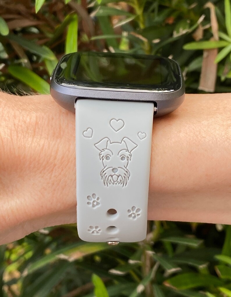 May include: A gray silicone watch band with a white silhouette of a dog and paw prints. The band is designed for a smartwatch.