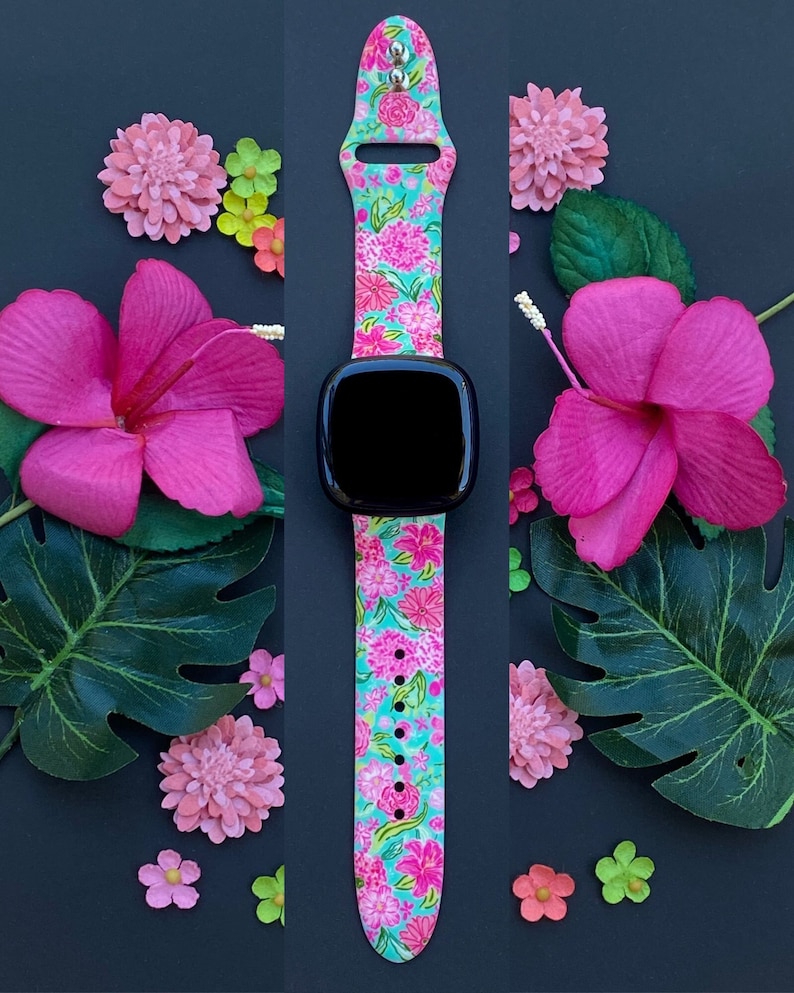 Op de afbeelding: Een horlogeband met bloemenprint met roze en groene bloemen op een turquoise achtergrond. De band is gemaakt van siliconen en heeft een zwart horlogeglas.