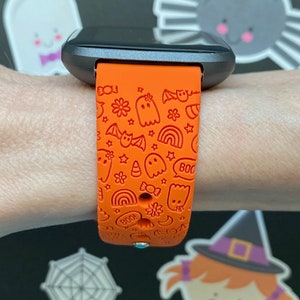 Puede incluir: Pulsera de reloj de silicona naranja con un dise&ntilde;o de tem&aacute;tica de Halloween. La pulsera presenta fantasmas, murci&eacute;lagos, estrellas, arco&iacute;ris, ma&iacute;z dulce y las palabras "&iexcl;Boo!" y "&iexcl;Boo!"