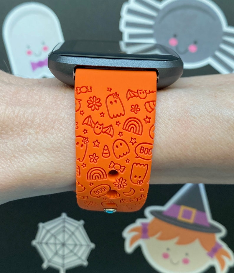 Puede incluir: Pulsera de reloj de silicona naranja con un dise&ntilde;o de tem&aacute;tica de Halloween. La pulsera presenta fantasmas, murci&eacute;lagos, estrellas, arco&iacute;ris, ma&iacute;z dulce y las palabras "&iexcl;Boo!" y "&iexcl;Boo!"
