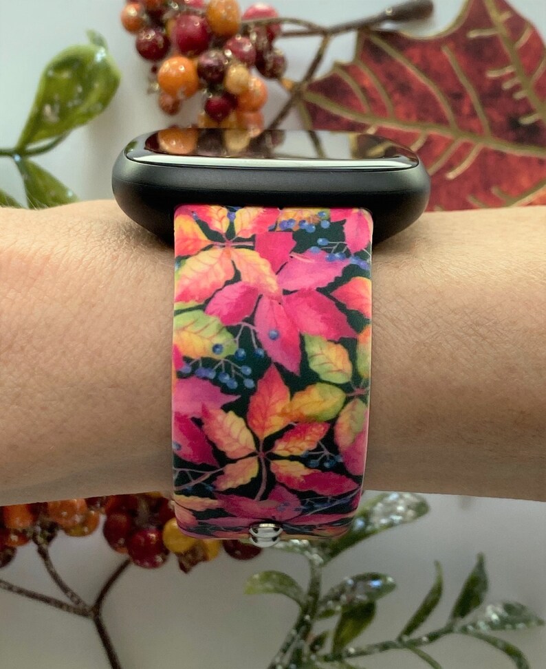 May include: A pink and orange watch band with a fall leaf pattern. The band is made of silicone and has a black watch face.
