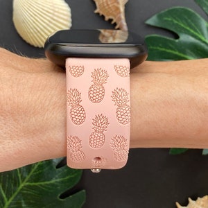 May include: A pink silicone watch band with a pineapple pattern. The band is designed for a smartwatch and has a black watch face.