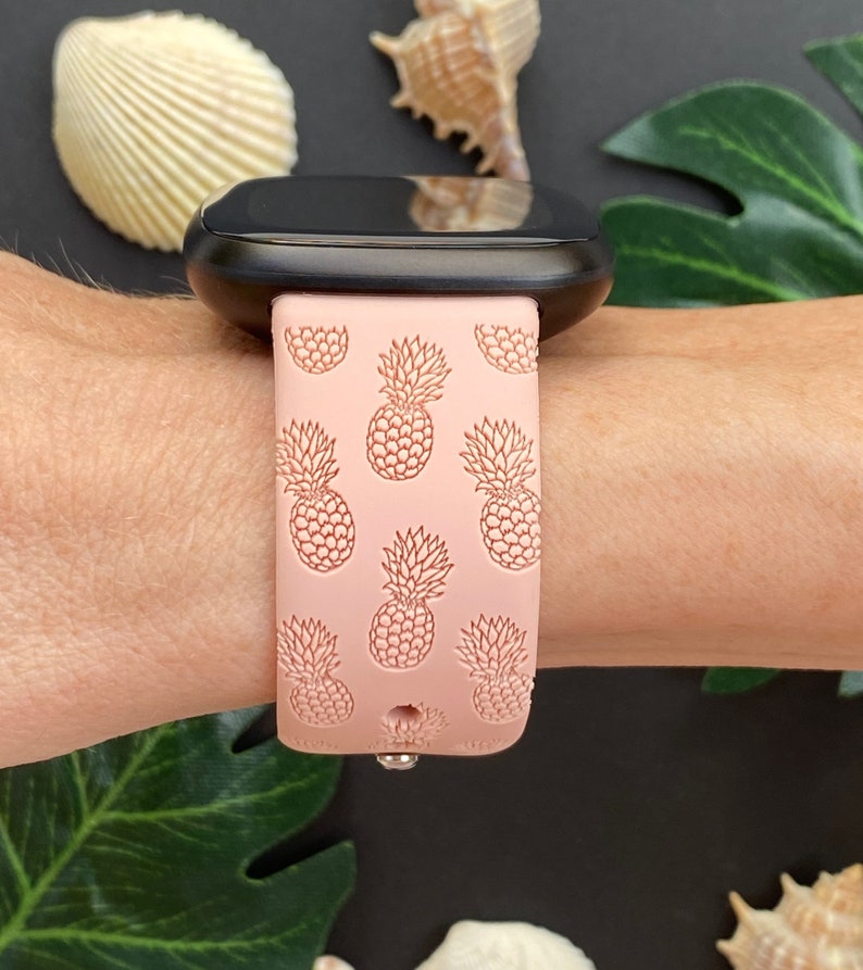 May include: A pink silicone watch band with a pineapple pattern. The band is designed for a smartwatch and has a black watch face.
