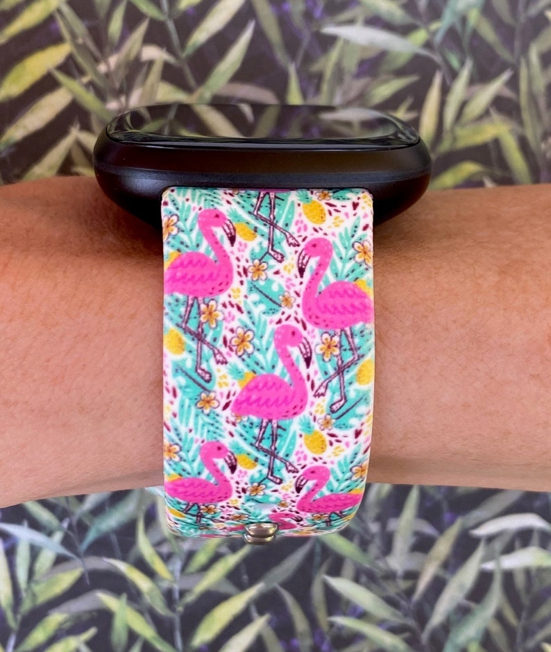 May include: A black smartwatch with a pink flamingo and tropical leaf patterned band.