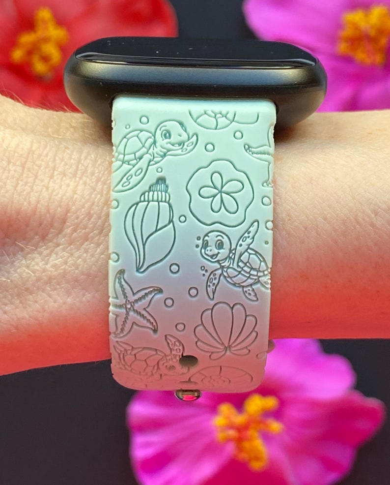 May include: A light green watch band with a sea life design. The band features embossed images of sea turtles, seashells, starfish, and other ocean-themed elements. The watch band is attached to a black watch.