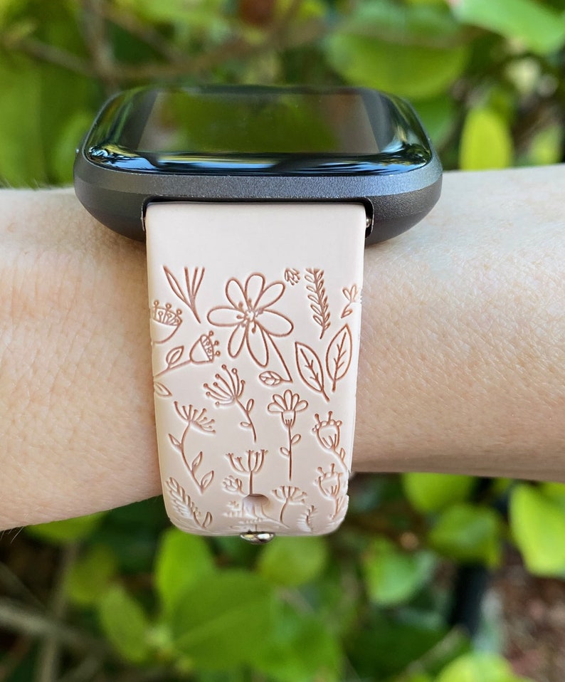Op de afbeelding: Een lichtroze smartwatchband met een bloemenpatroon. De band is gemaakt van siliconen en heeft een zwart horloge-scherm.