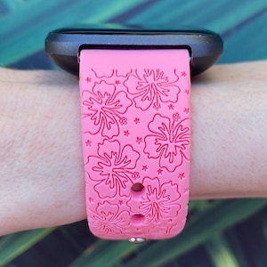 May include: A pink silicone watch band with a hibiscus flower pattern. The band is designed for a smartwatch and has a black watch face.
