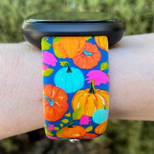 May include: A blue watch band with a pumpkin pattern. The band features orange, yellow, blue, and pink pumpkins on a blue background.