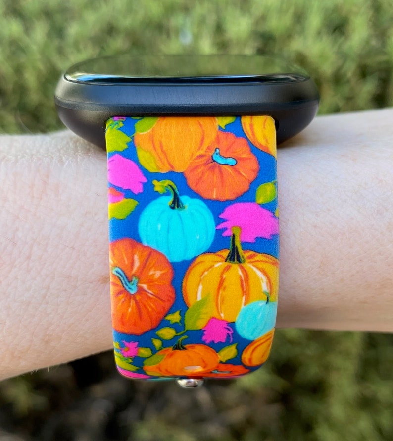 May include: A blue watch band with a pumpkin pattern. The band features orange, yellow, blue, and pink pumpkins on a blue background.