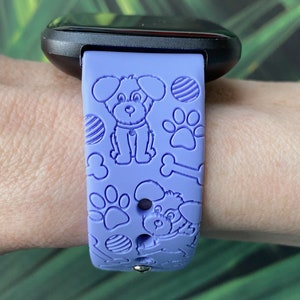 May include: A purple silicone watch band with a dog and bone pattern. The band is designed for a smartwatch.