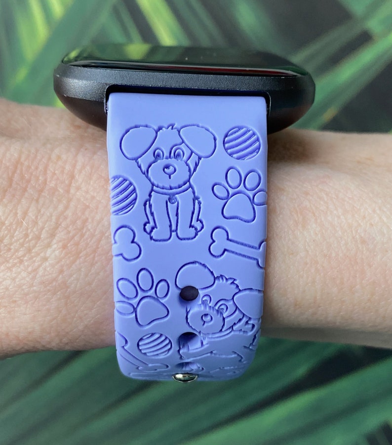 May include: A purple silicone watch band with a dog and bone pattern. The band is designed for a smartwatch.