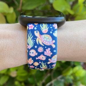 May include: A black smartwatch with a blue and pink patterned band featuring sea turtles, fish, and coral. The band has a colorful, whimsical design.