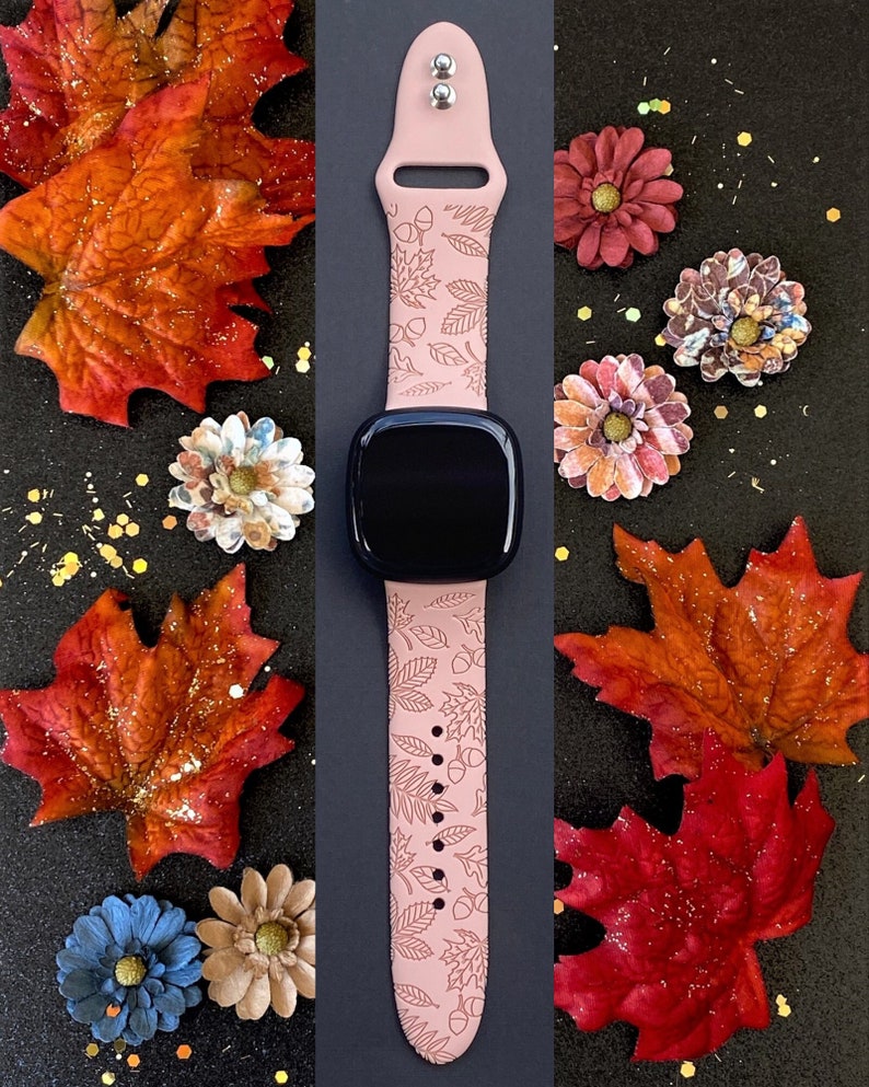 May include: A pink Apple Watch band with a fall-themed design featuring leaves and acorns. The band is made of silicone and has a smooth finish.