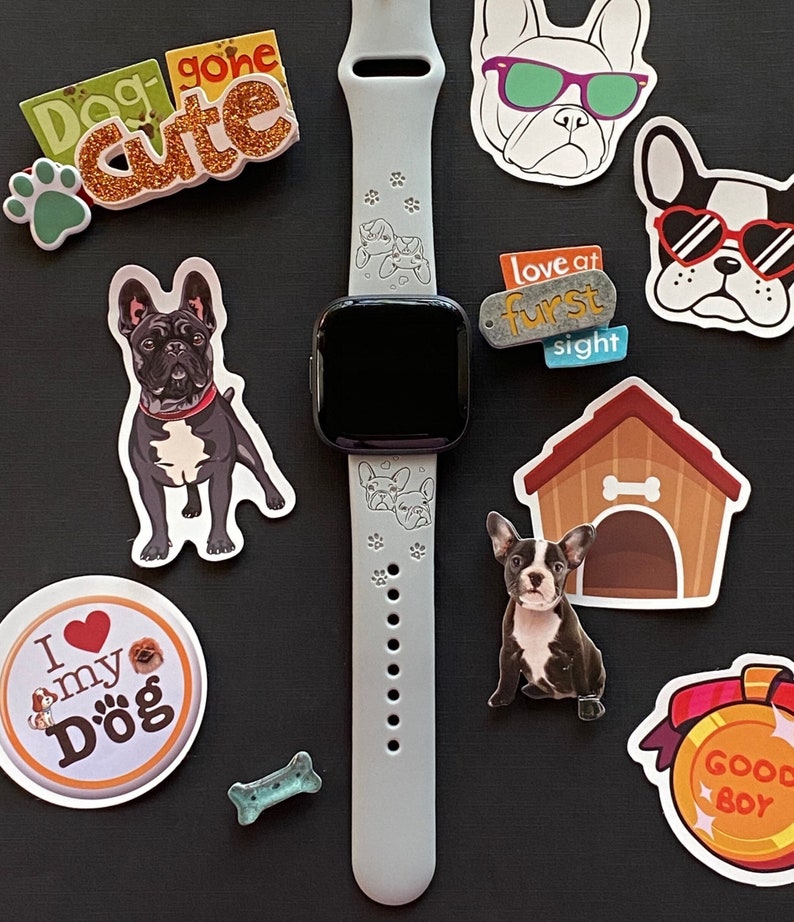 May include: A light gray silicone watch band with a black watch face. The band has paw prints and a dog silhouette design. The watch is surrounded by various dog-themed stickers, including "Dog gone cute", "Love at furst sight", and "Good Boy".