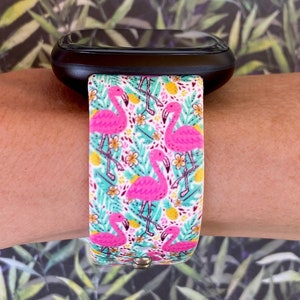 May include: A black smartwatch with a pink flamingo and tropical leaf patterned band.