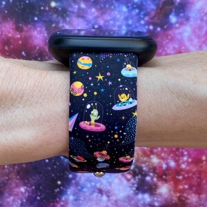 May include: A black smartwatch band with a colorful space-themed design featuring aliens in flying saucers, planets, and stars.
