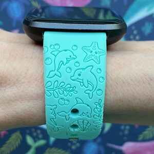 Puede incluir: Una correa de reloj de silicona azul turquesa con un dise&ntilde;o de delf&iacute;n, estrella de mar y algas marinas. La correa es compatible con un reloj inteligente.